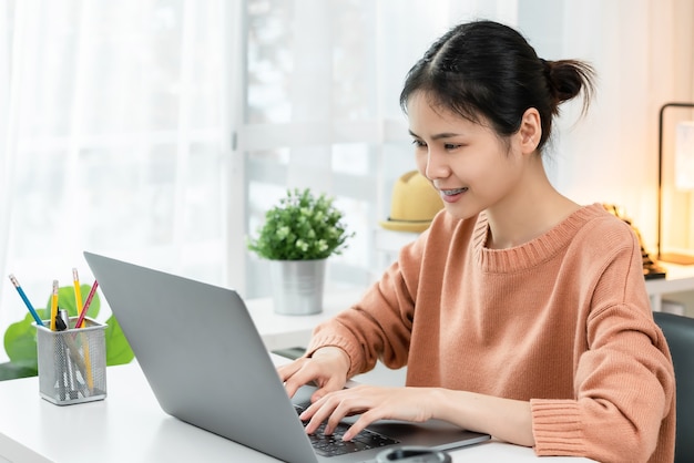 Smiley aziatische jonge vrouw met behulp van een laptop aan de tafel