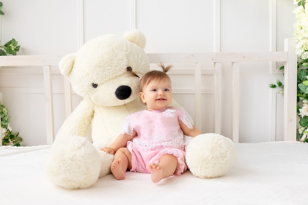 Smiley baby girl sitting on the bed with teddy bear