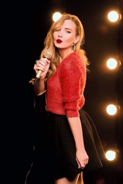 smiley beautiful woman with microphone singing song on the stage in karaoke