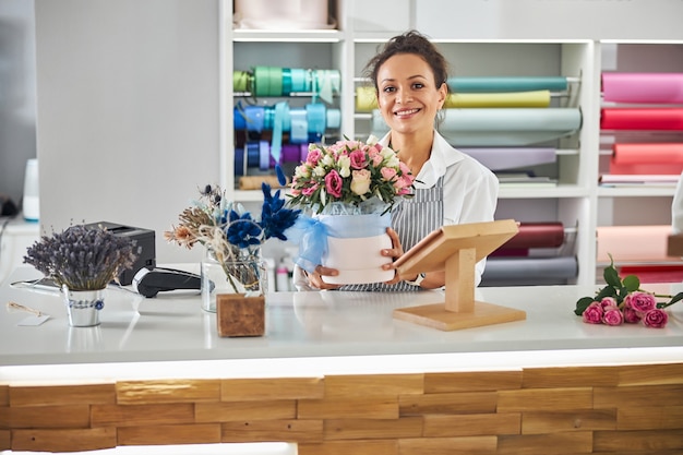 Smiley brunette bloemist poseren met een bloempot met rozen