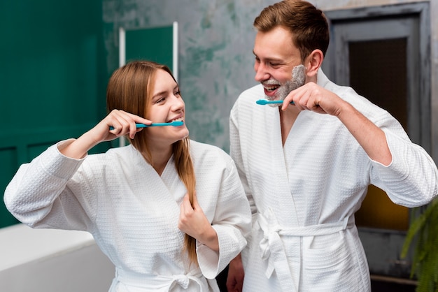 Photo smiley couple in bathrobes brushing their teeth