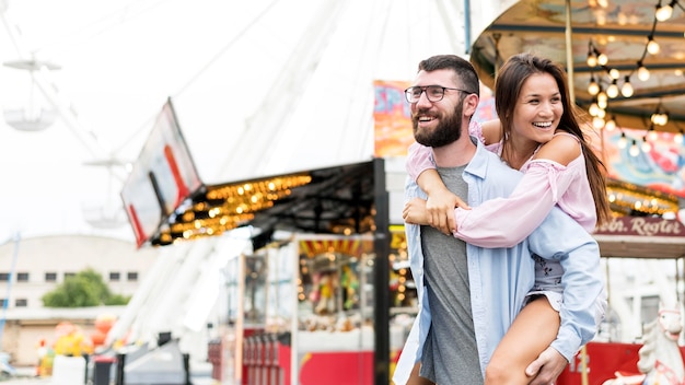 Coppia sorridente piggyback equitazione al parco di divertimenti