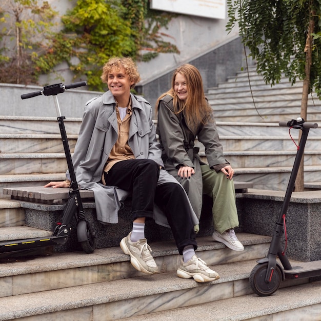 Smiley couple sitting next to electric scooters outdoors