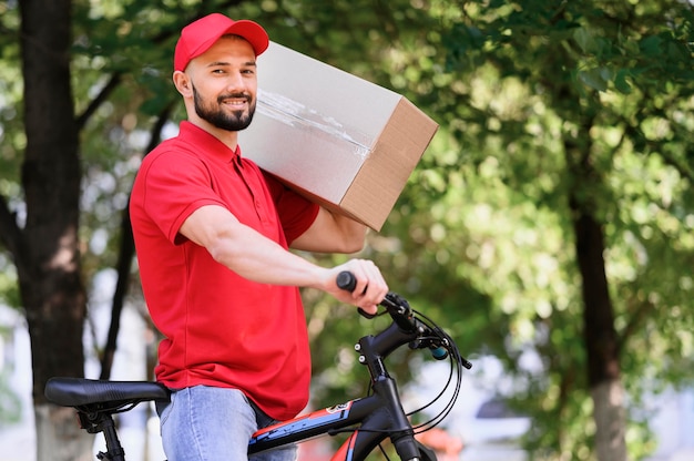 Photo smiley delivery man carrying parcel on a bike