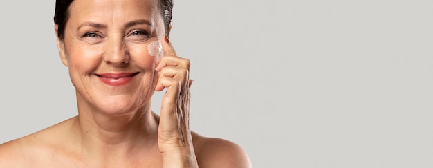 Photo smiley elder woman using moisturizer on her face