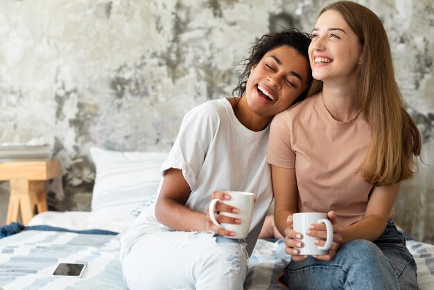 smiley female friends on bed with coffee
