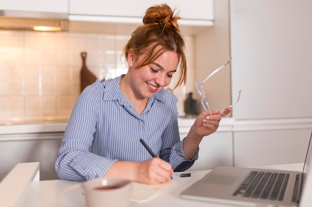 Photo smiley female teacher writing in agenda during online class
