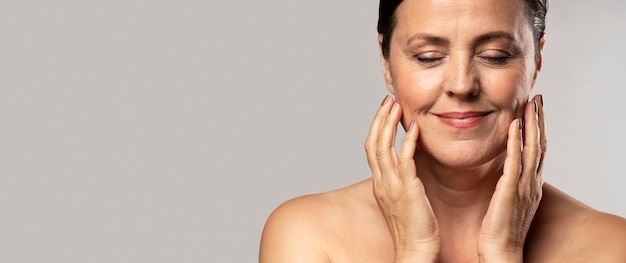 Smiley older woman with make-up on posing with hands on face and copy space