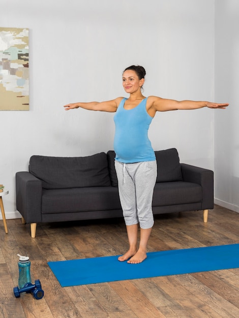 Smiley pregnant woman at home training on exercising mat