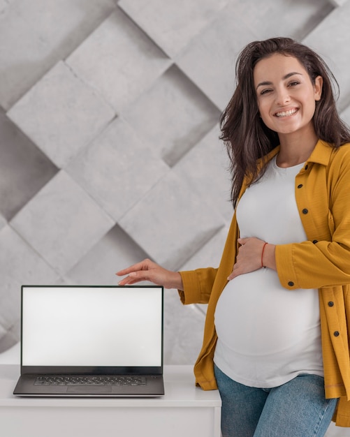 Donna incinta di smiley che posa con il computer portatile a casa
