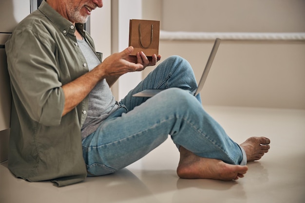 Photo smiley senior citizen showing gift bag to someone on video call