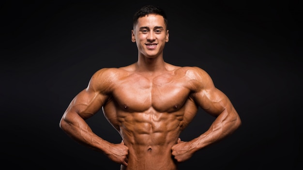 Smiley sportsman showing his muscles on black