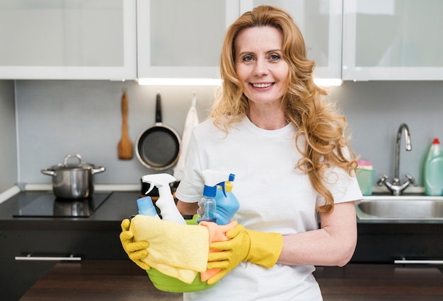 Smiley woman holding bucket of cleaning products