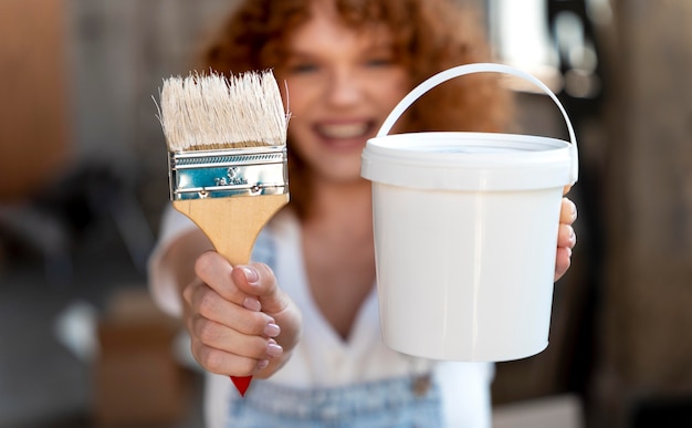 Photo smiley woman holding paintbrush and bucket for new home decoration