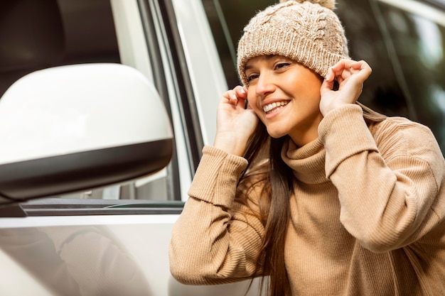 Photo smiley woman putting on beanie while on a road trip