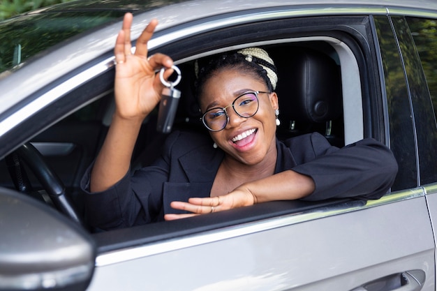 Photo smiley woman showing off keys to her car while sitting in it