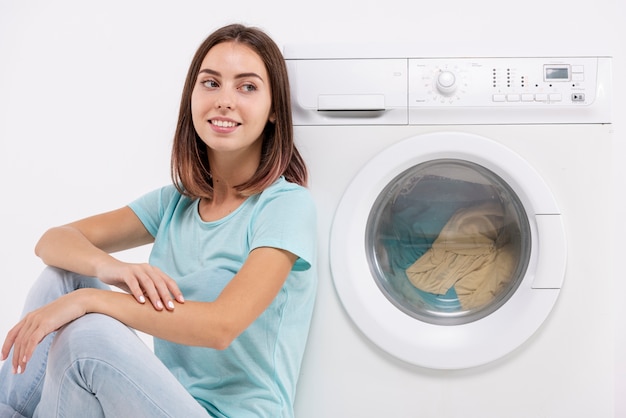 Photo smiley woman sitting near washing machine