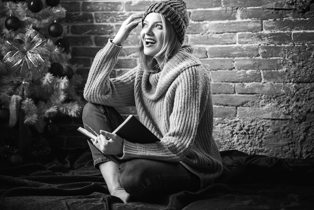 smiley woman in sweater next to Christmas tree