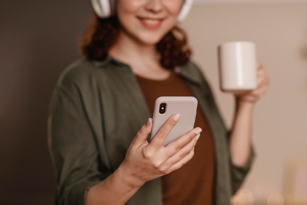 사진 커피를 마시면서 집에서 헤드폰으로 그녀의 스마트 폰을 사용하는 웃는 여자
