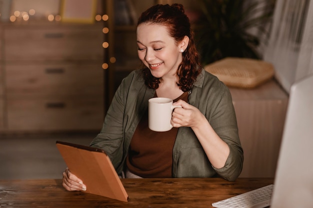 写真 コーヒーを飲みながら自宅でタブレットを使用してスマイリー女性