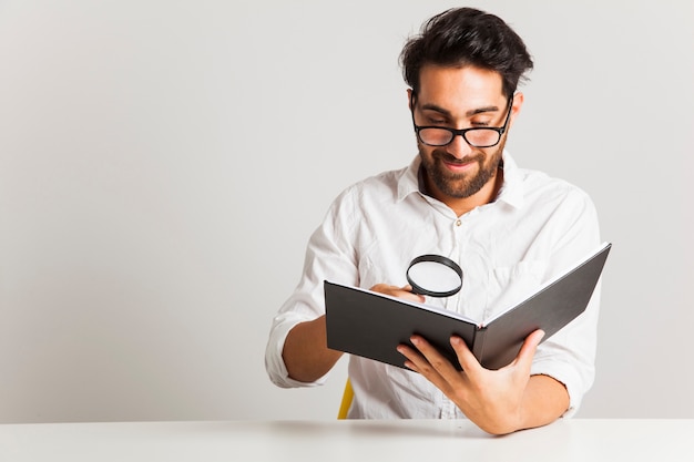 Photo smiley young man reading with loupe