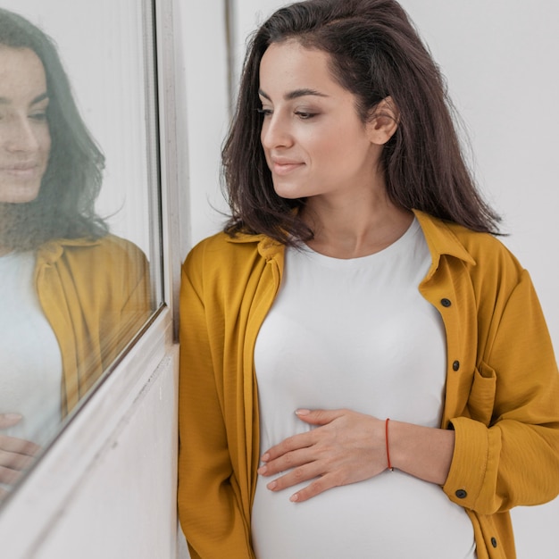 Smiley zwangere vrouw kijkt door raam