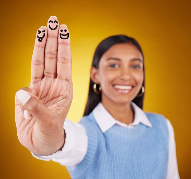 Foto smileyvingers en portret van indiase vrouw in studio voor kunstexpressie en plezier op gele achtergrond met kleurovergang handenkunst en tekenen door meisjesglimlach opgewonden en tevreden met emoji-gebaar of gezicht