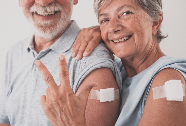 Smiling 70-year-old couple after receiving third dose of covid-19 coronavirus vaccine. Woman showing number three with her hand. Concept of protection and health care