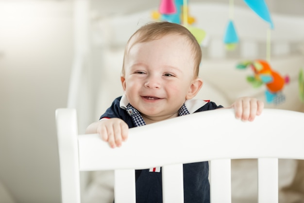 Smiling 9 month old baby standing in white wooden crib