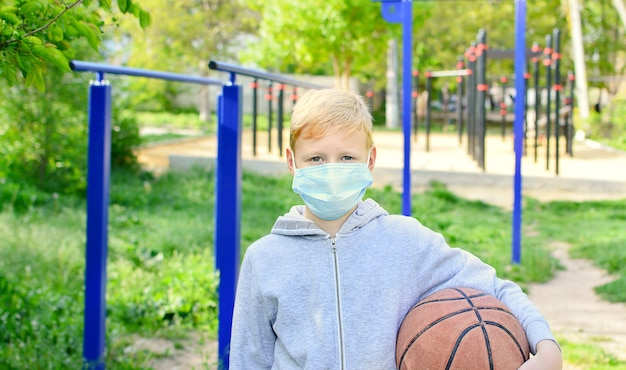 길거리에서 웃는 9 살 소년이 의료용 마스크를 벗고 공을 치고있다. 자가 격리 종료. 코로나 바이러스 감염병 유행.