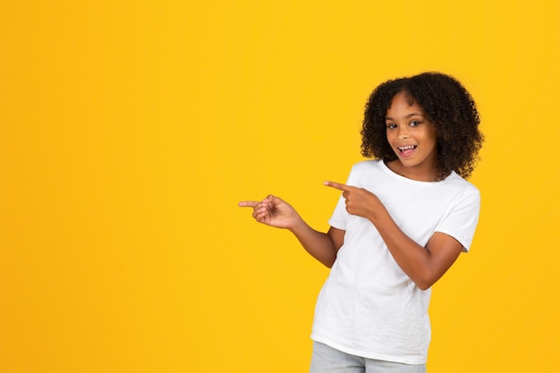 Фото Улыбающаяся кудрявая африканская американка-подросток в белой футболке указывает пальцем на пустое место