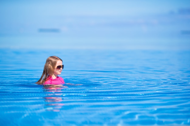 Smiling adorable girl having fun in outdoor swimming pool