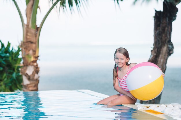 Smiling adorable girl playing with inflatable toy ball in outdoor swimming pool