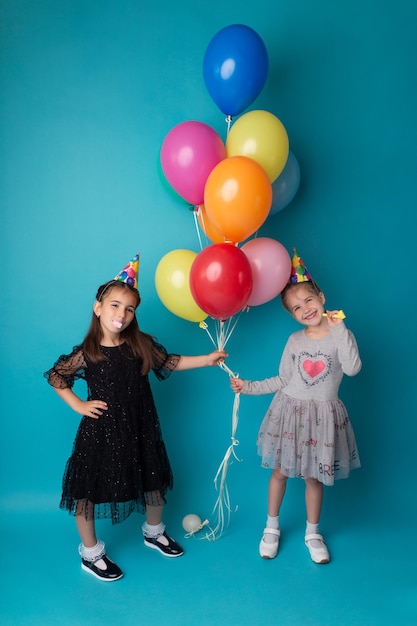 Smiling adorable little child girls posing with color air balloons on blue background