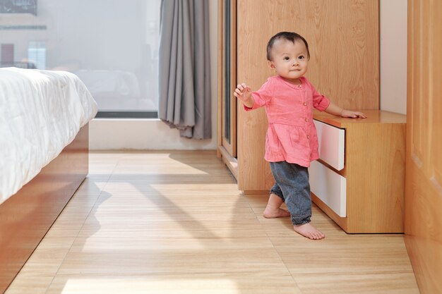 Smiling adorable little girl exploring apartment and walking in bedroom of her parents