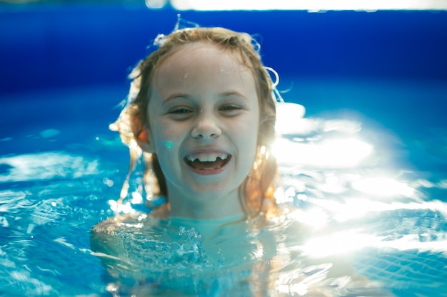 Smiling adorable seven years old girl playing and having fun in inflatable pool.