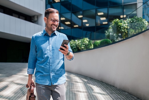 Smiling adult businessman receiving a lovely message on his phone while walking