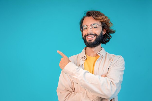 写真 笑顔の成人男性がコピースペースの青い背景に指を指して製品を紹介します