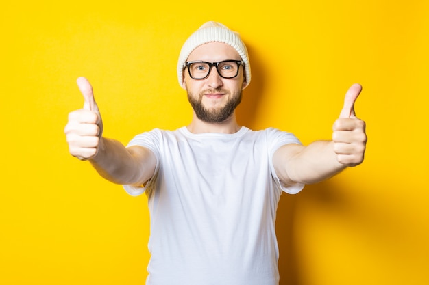 Smiling affable young guy with a beard in a cap and glasses shows a gesture with his hands