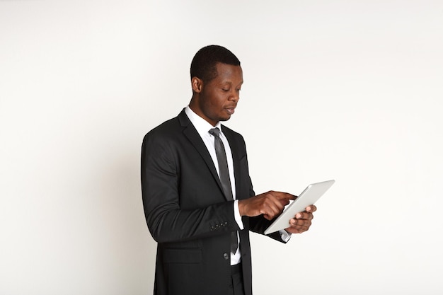 Smiling african american businessman using tablet. Young man in suit working with portable computer, isolated on white background. Business and modern technologies concept