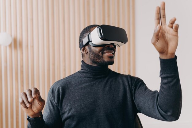 Smiling african american businessman in VR glasses sits in office testing virtual reality goggles