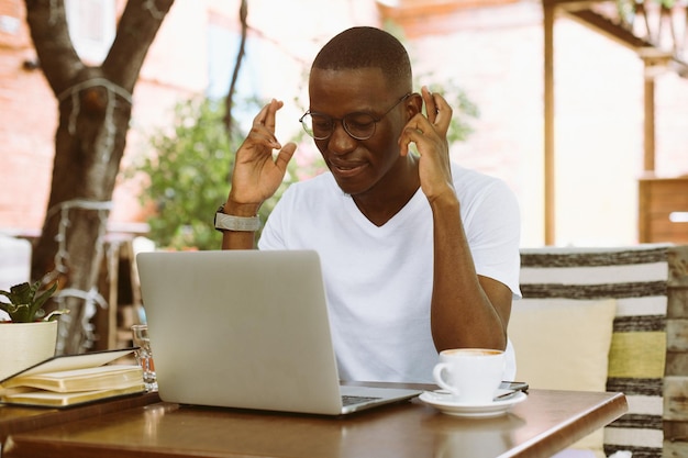 Улыбающийся афроамериканский бизнесмен работает на ноутбуке в кафе, скрещивая пальцы, желает удачи Заключение контракта
