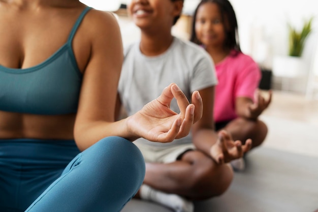 Smiling African American children and their fit mother sitting in lotus pose exercising at home
