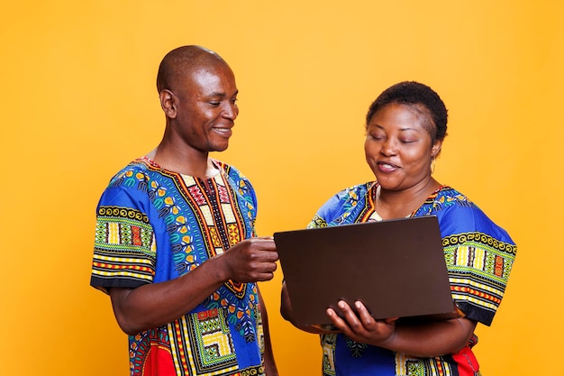 Smiling african american couple using laptop and giving debit card information for online purchase at checkout Cheerful man and woman standing with portable computer and paying on internet