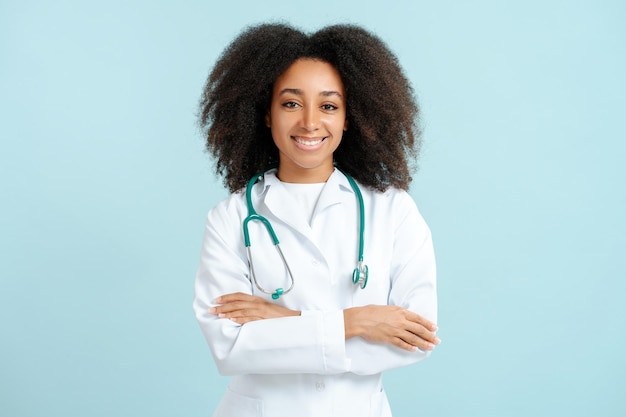 Photo smiling african american doctor in white coat with stethoscope and crossed arms looking at camera