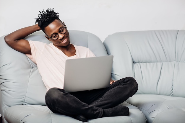 ソファにノートパソコンと一緒に座ってメガネで笑顔のアフリカ系アメリカ人の男