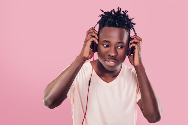 Smiling African-American man in headphones listening to music on pink background