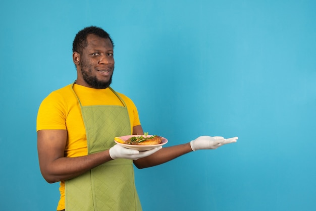 A smiling African American man holding meal in one hand , stands over blue wall. 