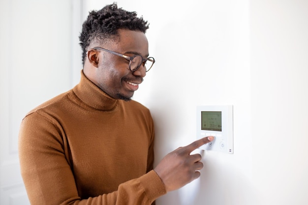 Uomo afroamericano sorridente che utilizza il moderno controller del sistema di casa intelligente sul muro giovane positivo