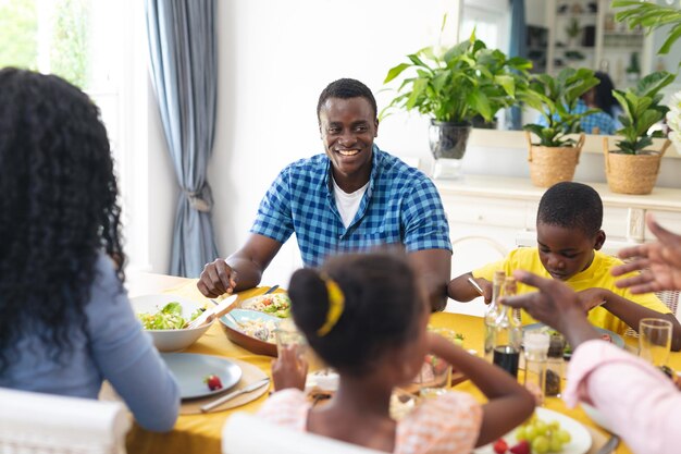 Foto sorridente uomo afroamericano di mezza età che pranza con la famiglia a casa il giorno del ringraziamento. inalterato, famiglia, cibo, insieme, culture e concetto di vacanza.